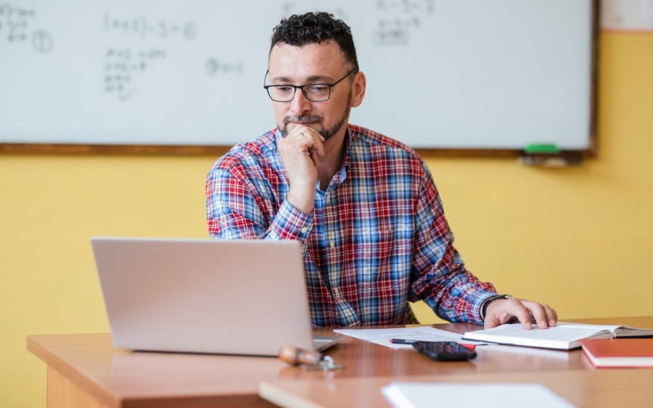 Teacher views laptop in classroom