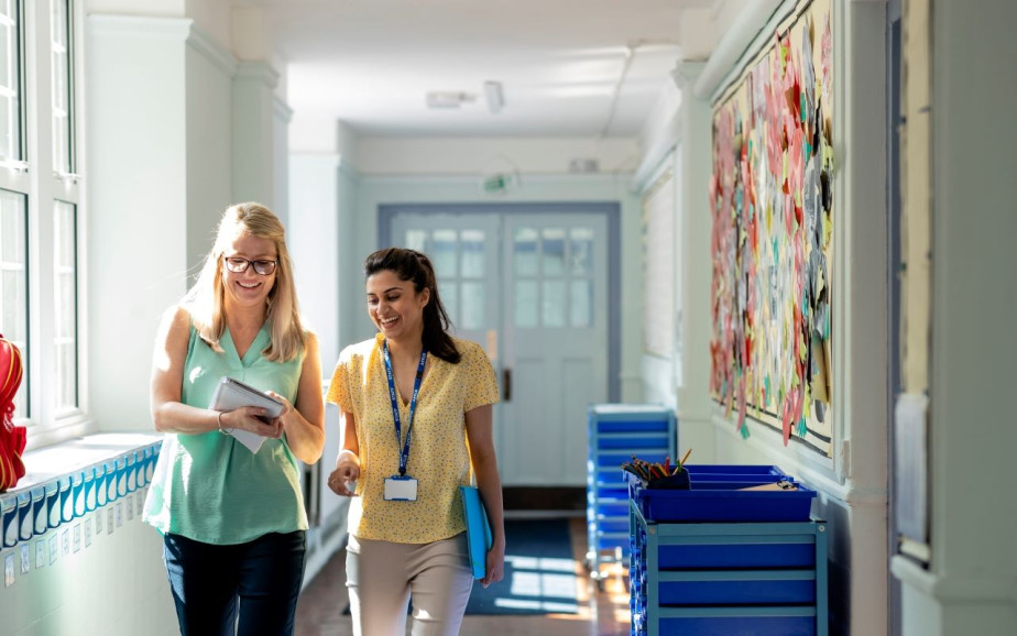 Two female teachers walk in a school hallway.