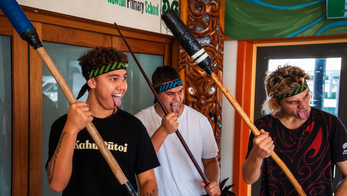 Three boys performing with mau rakau