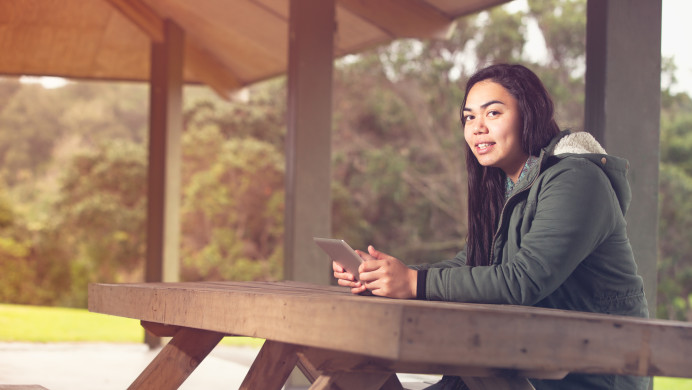 A young person sits at a park table with their phone.
